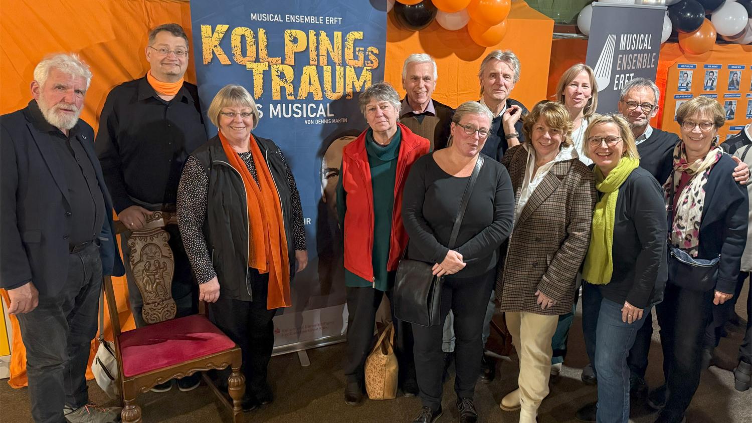 Vorstandsmitglieder stehen vor einem Musicalbanner, mit Luftballons in orange und schwarz.